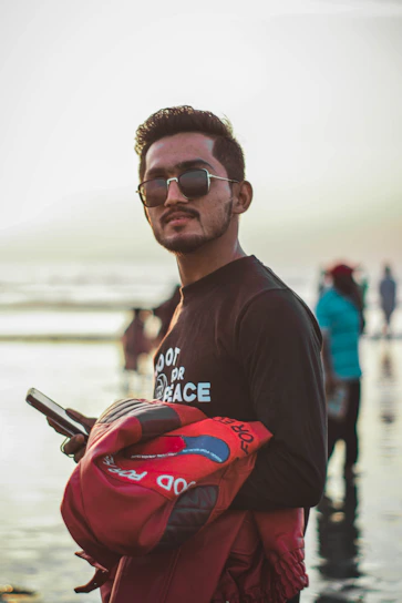 A stylish man wearing a District Beach jacket standing by the waterfront at sunset, blending cityscape and coastal elements.