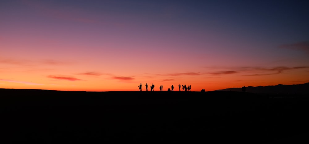 a group of people standing on top of a hill at sunset