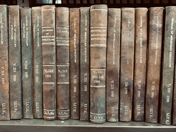 A collection of old, leather-bound volumes of the 'Journal of Molecular Structure' is arranged side by side on a shelf. Each book spine displays the journal title, volume number, and publication year, with years ranging from 1989 to 1990.
