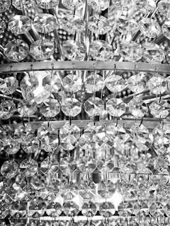 An intricate arrangement of crystal or glass beads, intricately connected by metal hooks, creates a dazzling and reflective surface. The circular facets of the beads capture and refract light, producing a sparkling effect.
