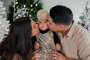 a man and woman kissing a baby in front of a christmas tree