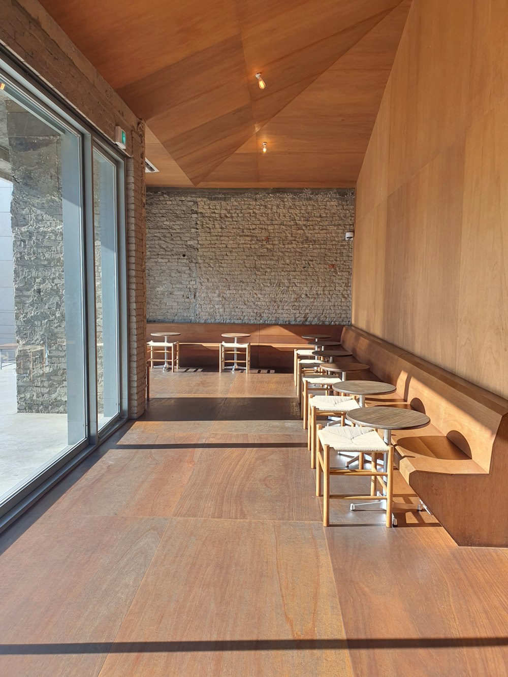 um restaurante com mesas e cadeiras de madeira ao lado de uma grande janela
