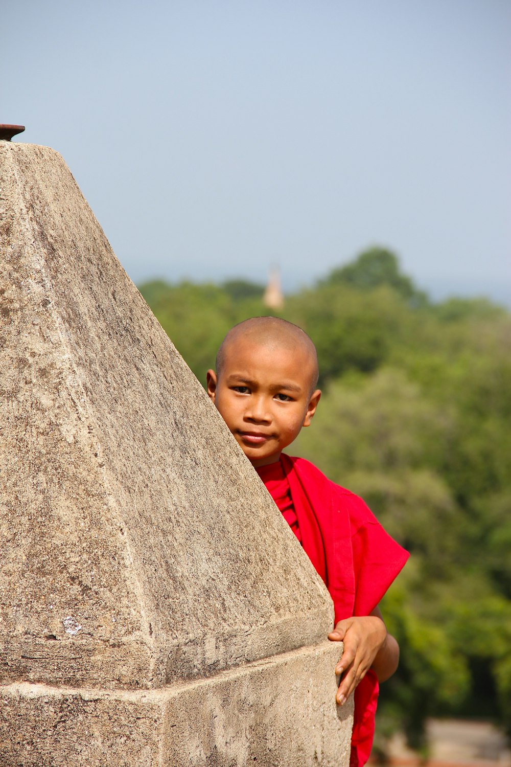 a young boy in a red shirt leaning against a stone pillar