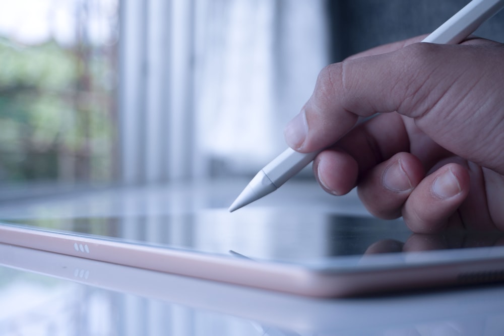 a person holding a pen and writing on a tablet