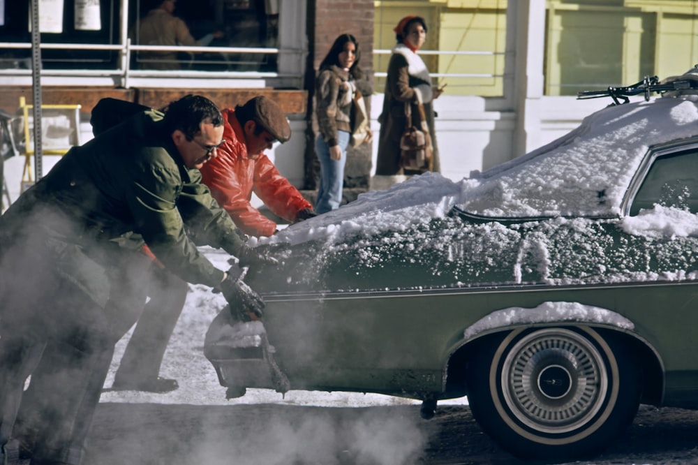a group of people standing around a car covered in snow