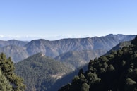 A panoramic view from a mountain summit overlooking layered forests and distant peaks.