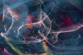 Swirling and ethereal, the image presents a blend of smoky, wispy forms in a dynamic mix of colors. Streaks of orange, pink, and blue intertwine over a dark background, creating an intriguing abstract pattern reminiscent of swirling smoke or light trails.