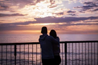 A couple relaxing at a cozy hotel balcony overlooking a sunset.