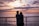 A happy couple standing on their oceanfront balcony at sunset, overlooking the waves.