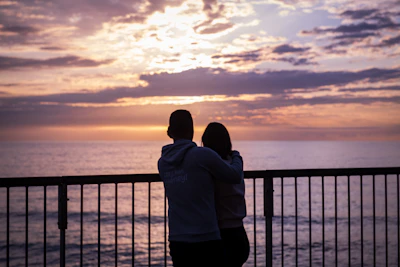 A romantic couple embracing on a hotel balcony overlooking the ocean at sunset.