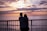A happy couple standing on a balcony overlooking the Baltic Sea at sunset.