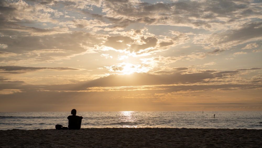 a person sitting on a beach watching the sun set