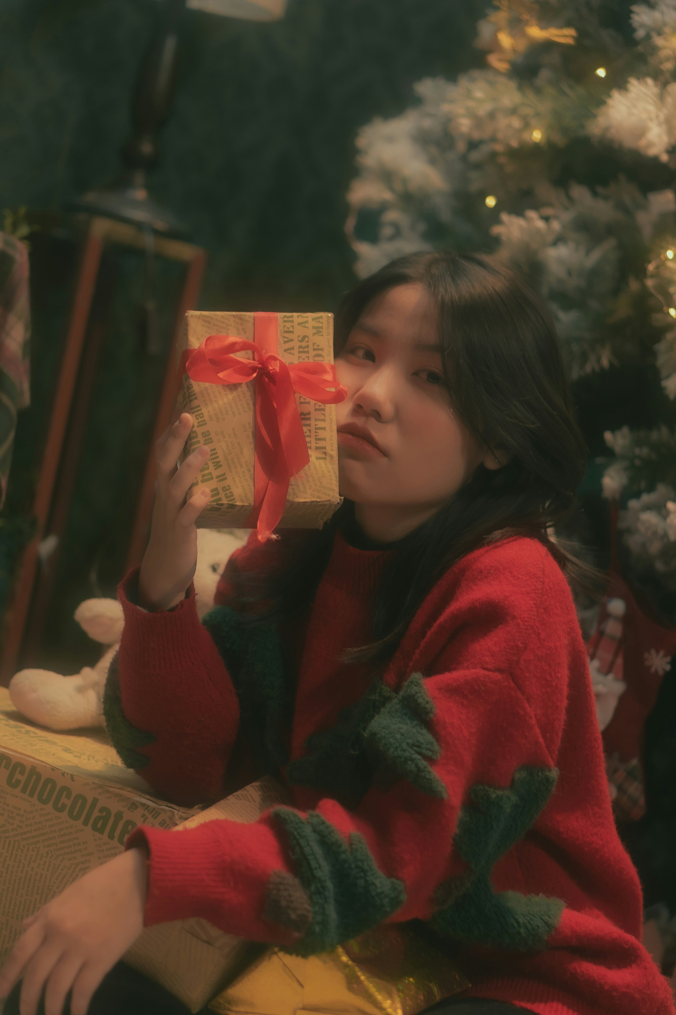 a young girl sitting in front of a christmas tree holding a present