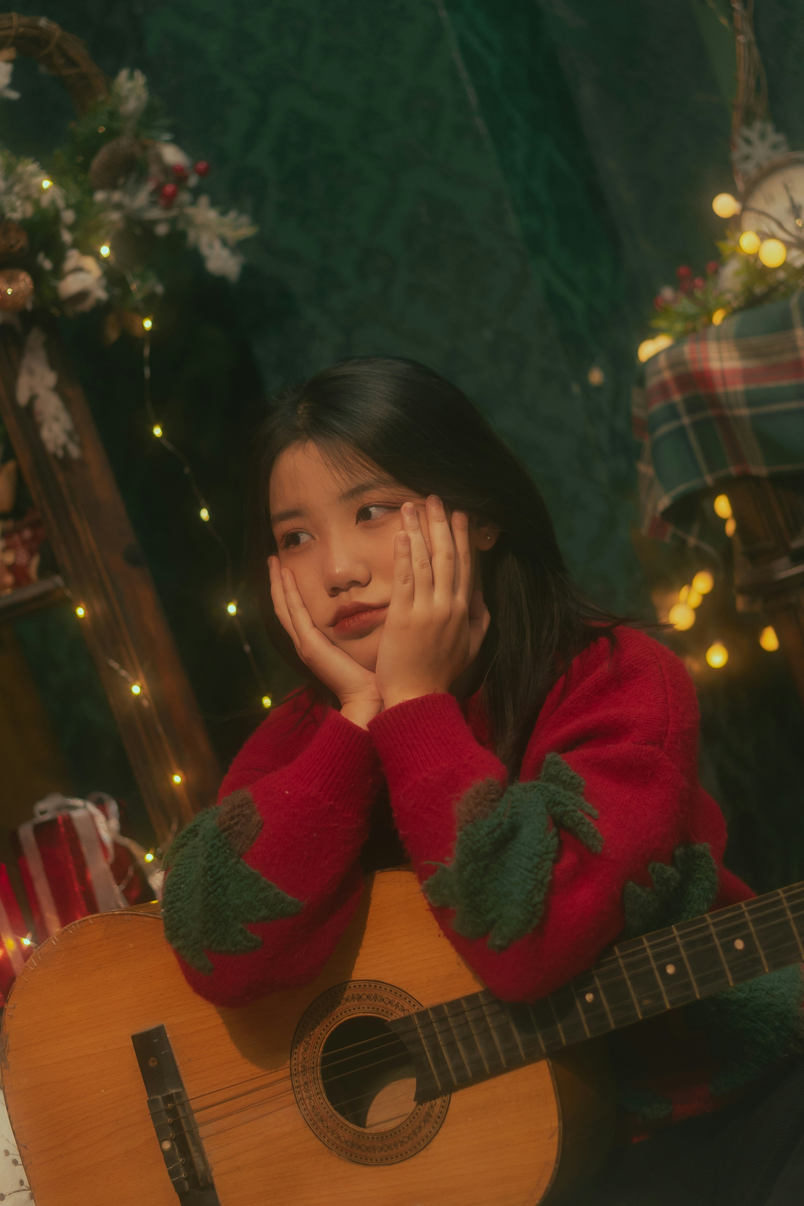 a young girl sitting in front of a christmas tree holding a guitar