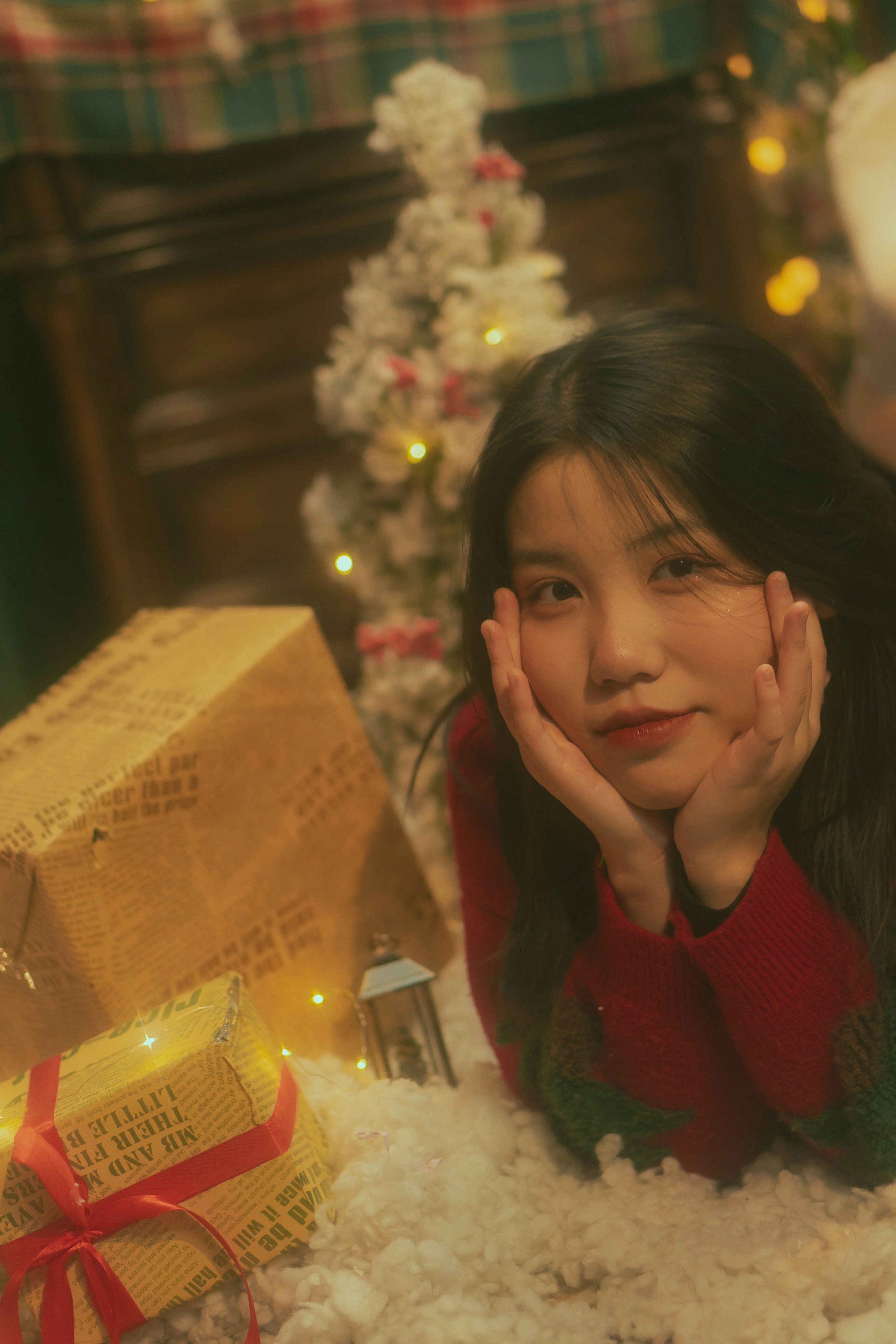 a young girl laying on a pile of snow next to a christmas tree