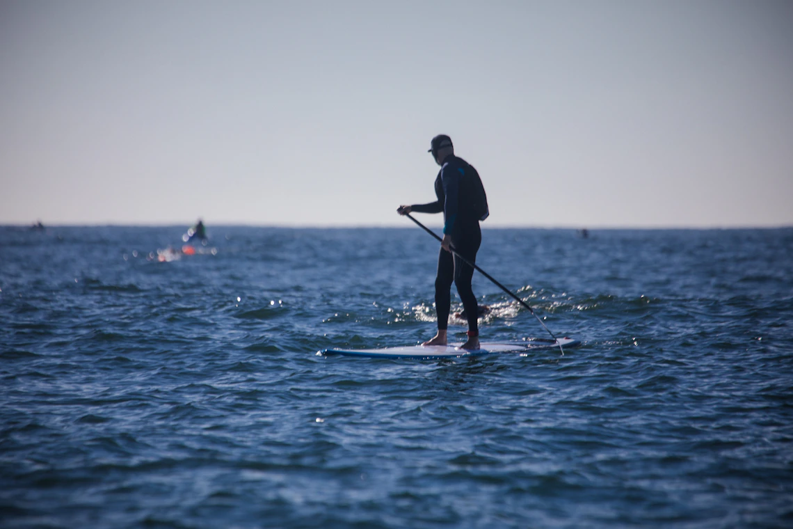 Stand-up paddleboarder crossing sunlit coastal water