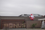 A large inflatable Santa Claus is positioned on the roof of a building. The facade features a sign that reads 'BONUS' illuminated with lights. There are two decorated Christmas trees on either side, adding to the festive theme.