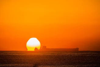 Workers coordinating the loading of cargo onto a large vessel at sunset.