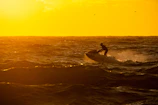 Jetski riders performing tricks over sparkling waves at sunset.