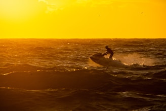 A vibrant red jet ski skimming across sparkling ocean waves at sunset.