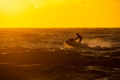 A vibrant red jet ski skimming across sparkling ocean waves at sunset.