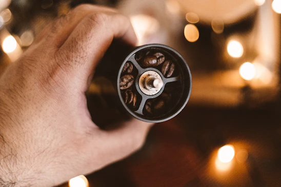 Hands expertly grinding coffee beans beside a camera setup capturing the process in warm, inviting light.