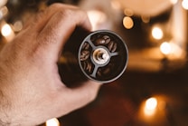 A hand holding a manual coffee grinder filled with coffee beans, with a warm, blurry background featuring soft light bokeh.
