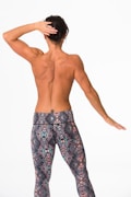 A person with a muscular build stands with their back facing the viewer, wearing patterned leggings. Their right hand is placed on the back of their head, while the left arm is extended slightly outward. The setting is a plain white background.