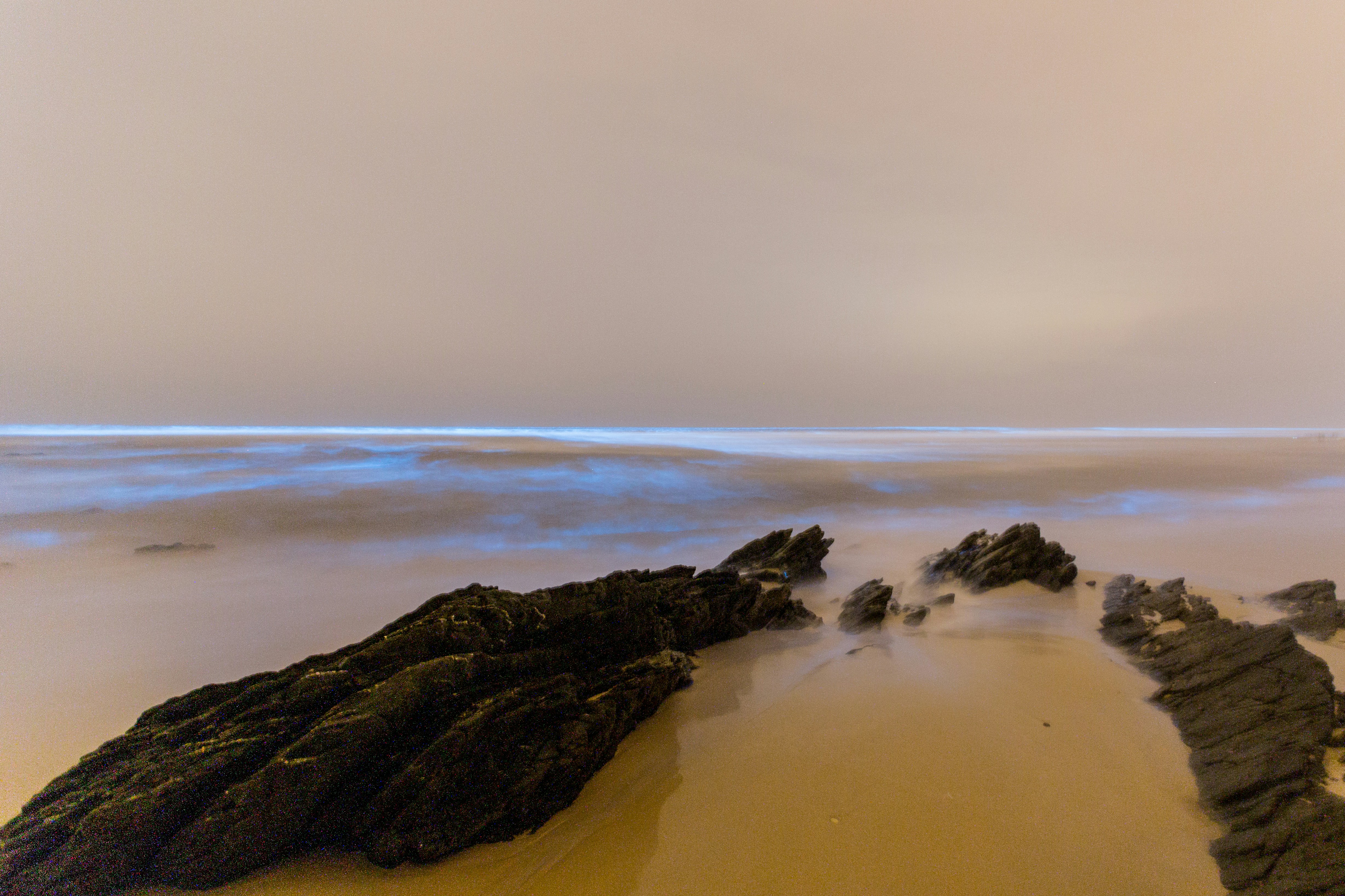 a sandy beach with rocks and water in the distance