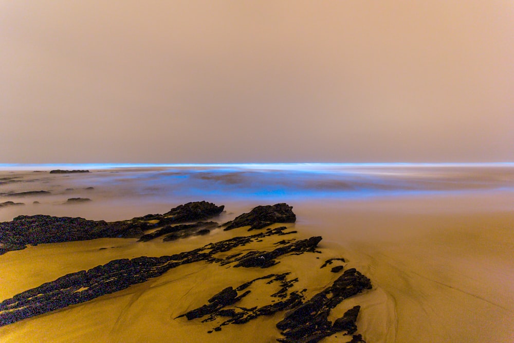 a sandy beach covered in lots of rocks under a cloudy sky