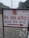 A sign with text written in Hindi, featuring a bank logo and an arrow. The sign is placed outdoors on a grassy area with some litter visible on the ground. In the background, there are trees and electrical poles with power lines stretching into the distance.