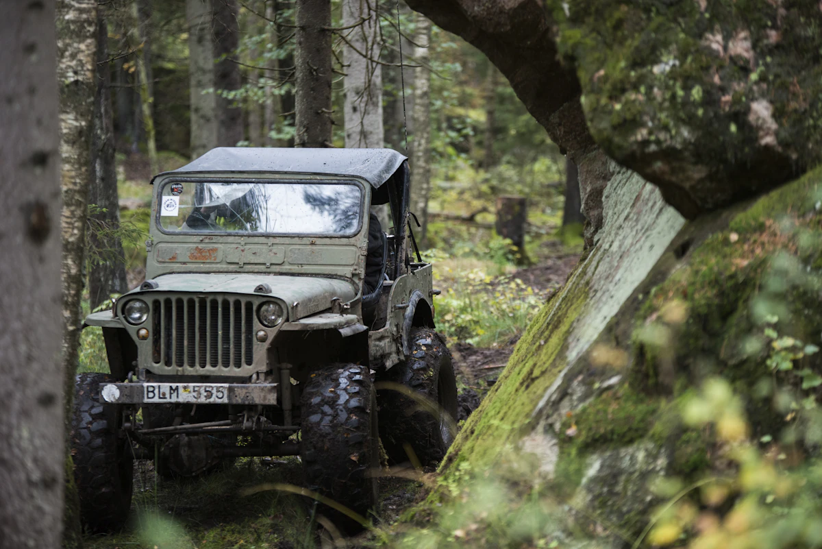 A vintage olive-green Willys Jeep, the classic Colombian mountain vehicle, on a forest trail
