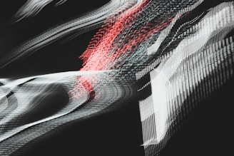 A dynamic and abstract composition with sweeping lines and blurred patterns, featuring interwoven textures of light. Pulsating red and white streaks create a sense of motion against a dark background, evoking a futuristic or digital aesthetic.