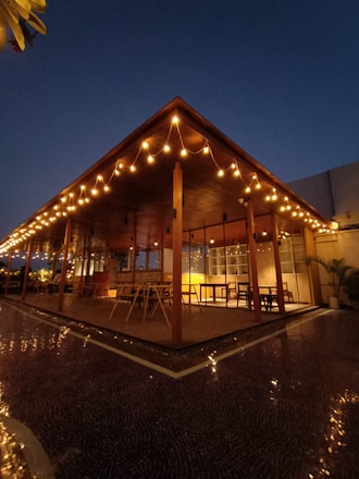 A cozy backyard illuminated by warm string lights draped over a wooden pergola at dusk.