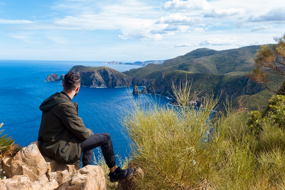 a man sitting on a rock looking out at the ocean