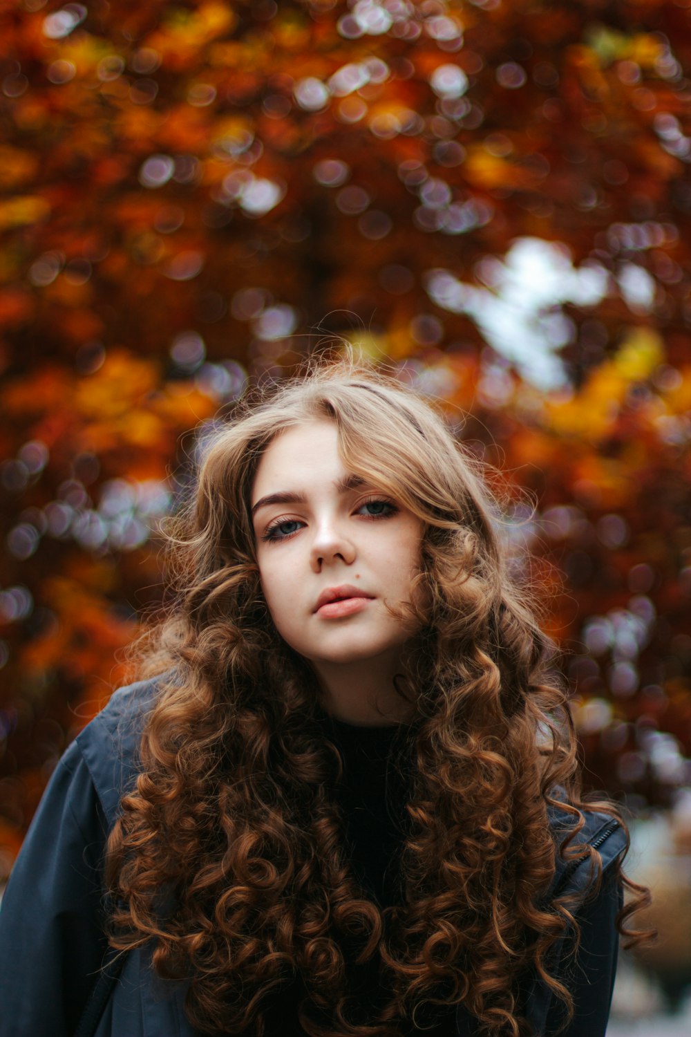 a woman with long curly hair standing in front of a tree