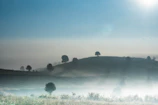 A panoramic view of rolling hills bathed in early morning light with a hint of fog.