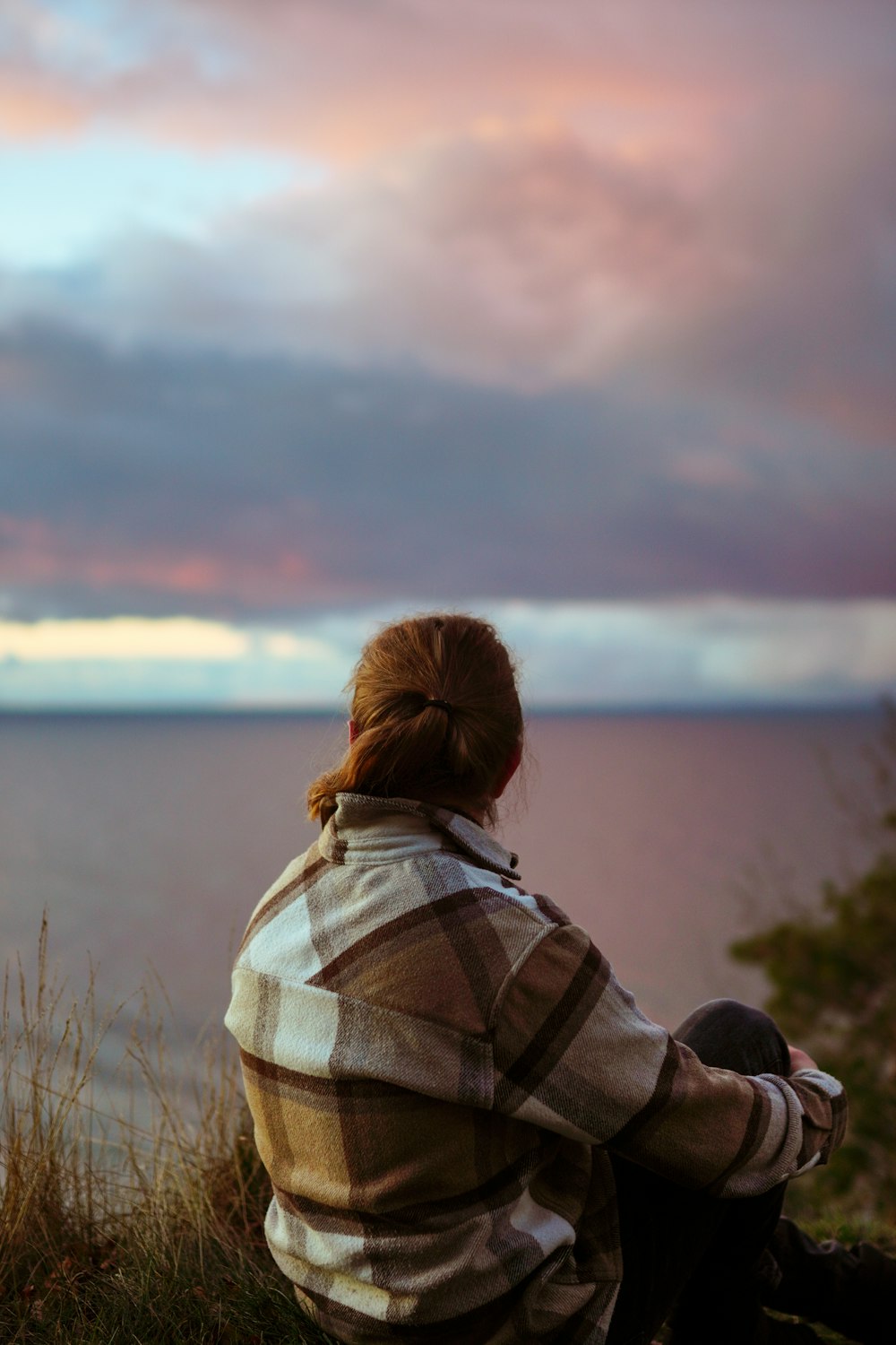 a woman sitting on top of a hill next to the ocean