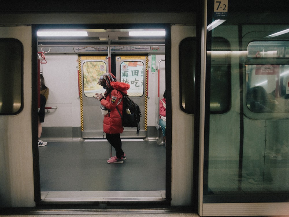 a woman in a red coat standing on a subway