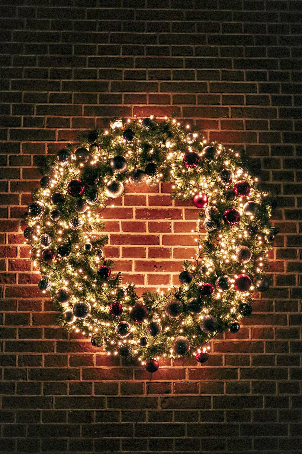 a lighted christmas wreath on a brick wall