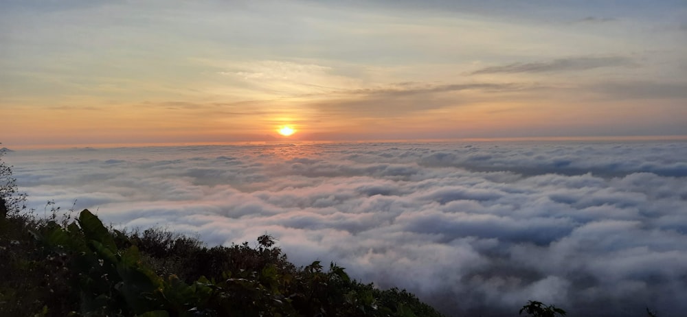 the sun is setting over a sea of clouds