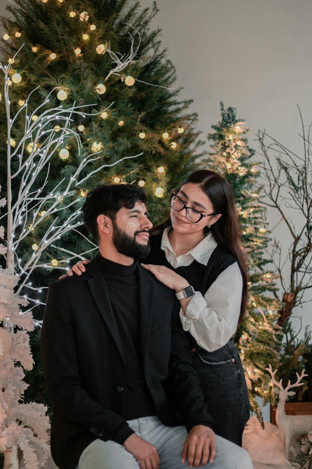 a man and woman sitting next to a christmas tree