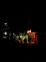 A moody city street at night bathed in deep red neon glow with silhouettes of lone wanderers.