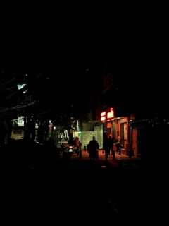 A cinematic shot of a deserted street at night, bathed in deep shadows and red neon lights.