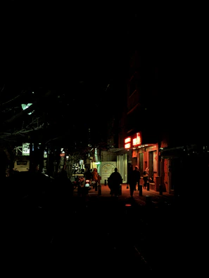 A moody city street at night bathed in deep red neon glow with silhouettes of lone wanderers.
