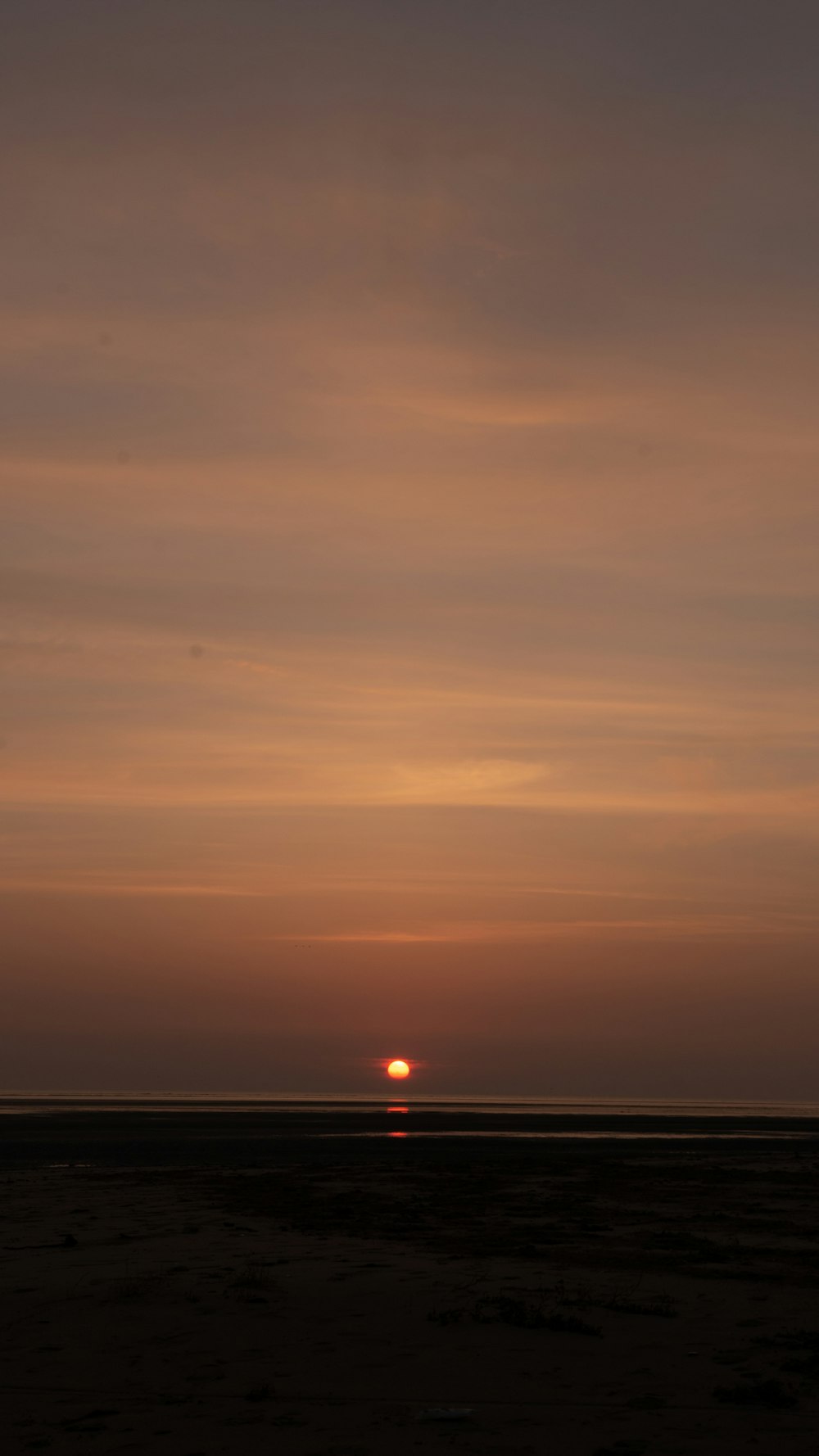 the sun is setting on the horizon of a beach