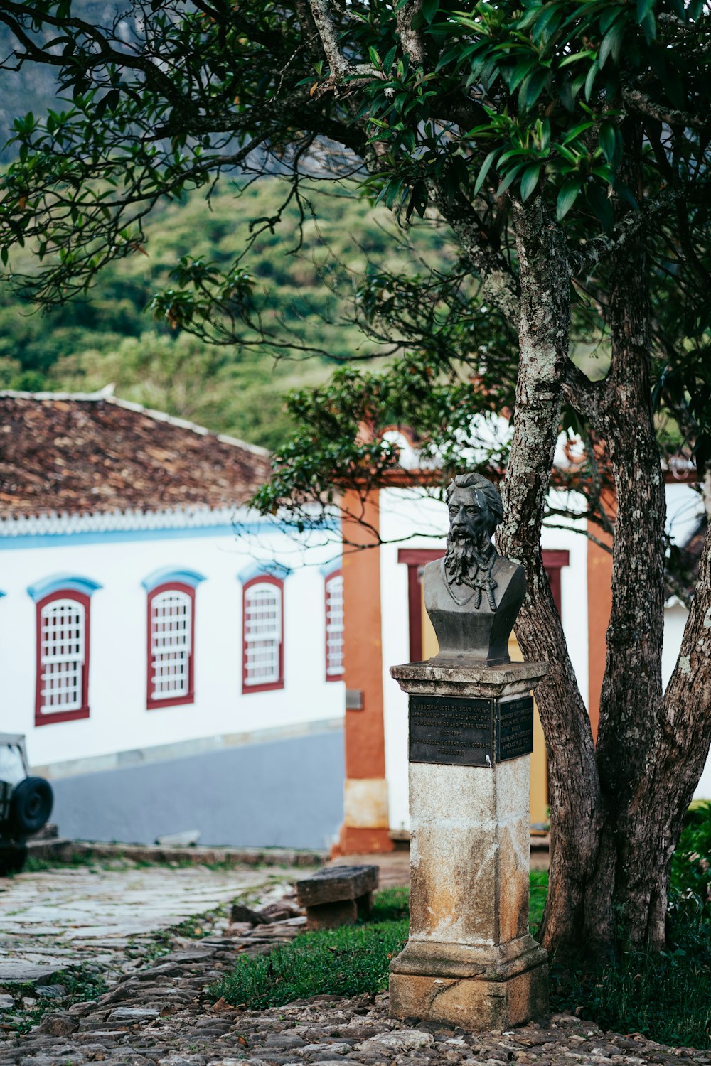 a statue in front of a tree on a cobblestone street