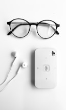 A pair of round black-rimmed eyeglasses, a pair of white earphones, and a white portable Wi-Fi router labeled '4G' are neatly arranged on a plain white background.