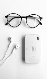 A pair of round black-rimmed eyeglasses, a pair of white earphones, and a white portable Wi-Fi router labeled '4G' are neatly arranged on a plain white background.