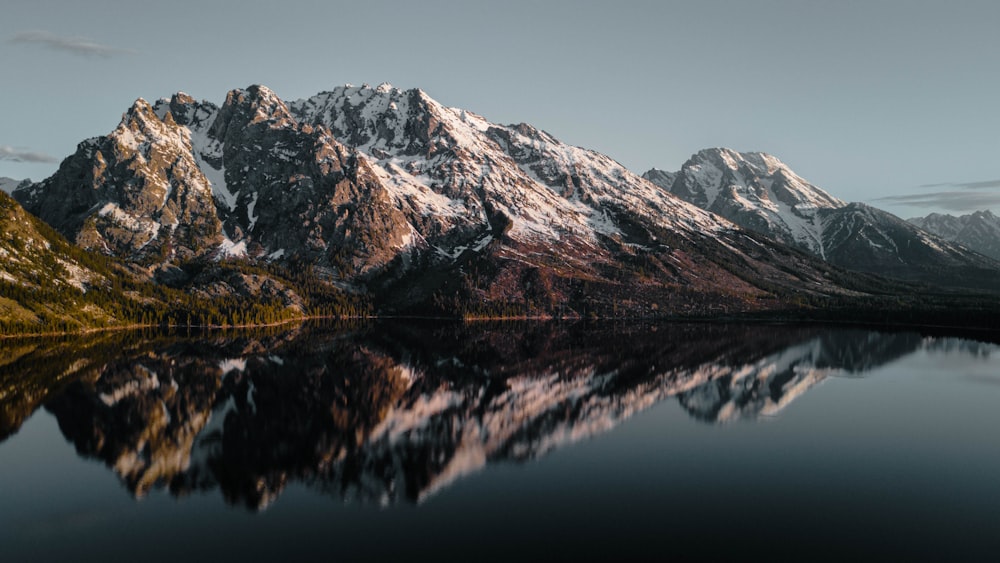 a mountain range is reflected in the still water of a lake
